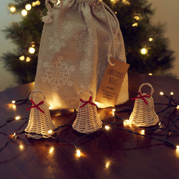 Three handmade rattan Christmas bells with red bows and kit bag under a Christmas tree